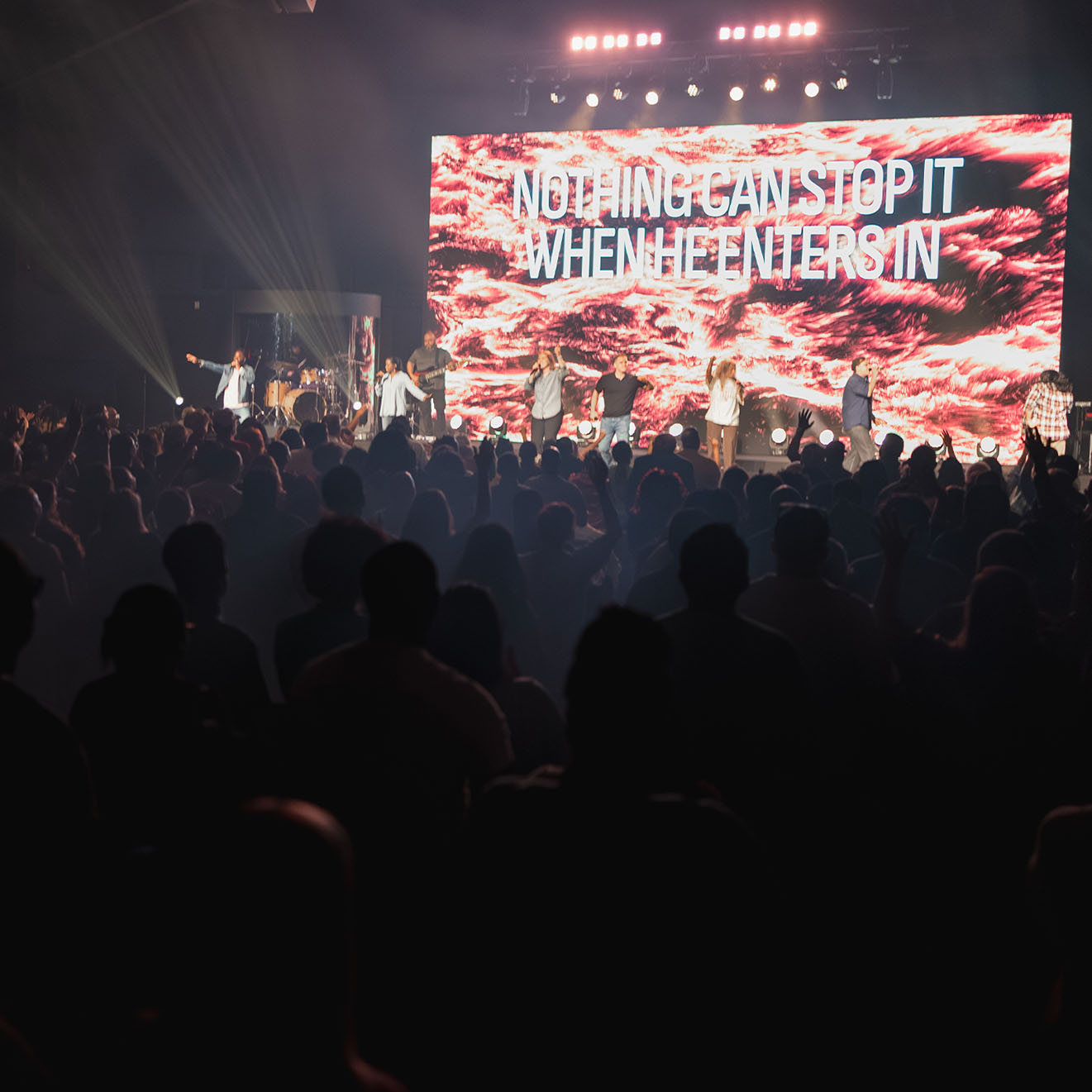 Crowd watching singers and musicians perform on stage with screen reading 'Nothing can stop it when he enters in.'