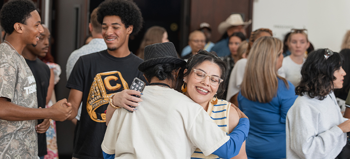People socializing and hugging in a crowded indoor gathering with diverse attendees.