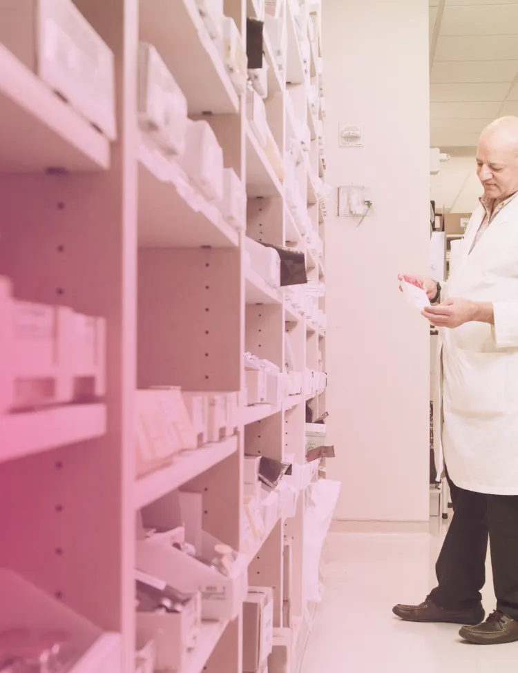 Pharmacist reviewing a prescription beside pharmacy shelves