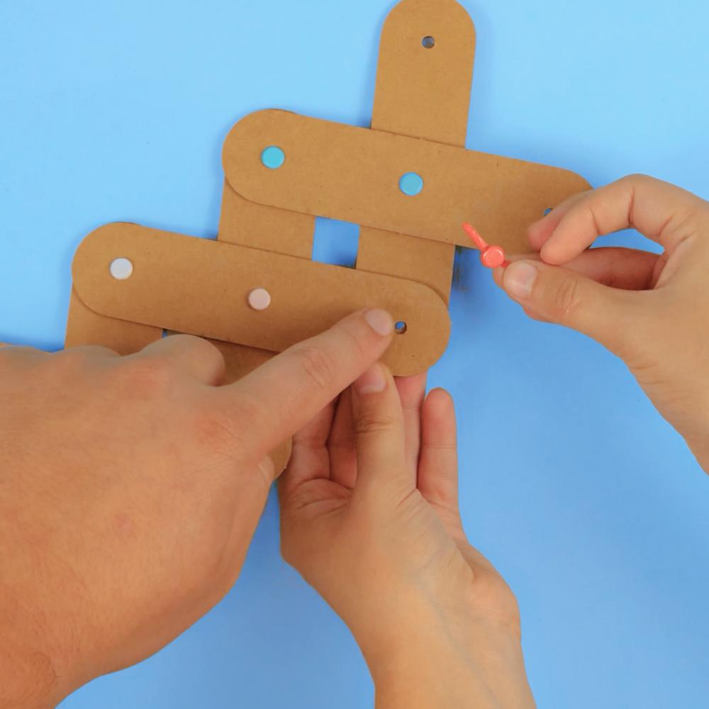 An adult's and a child's hands building an Art Machines cardboard creature together