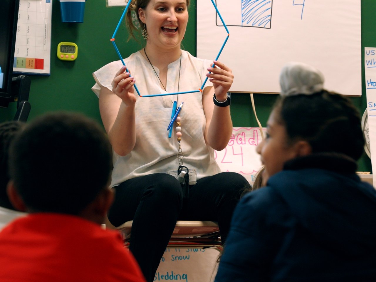 An educator holding up a straw hexagon for a class of seated learners