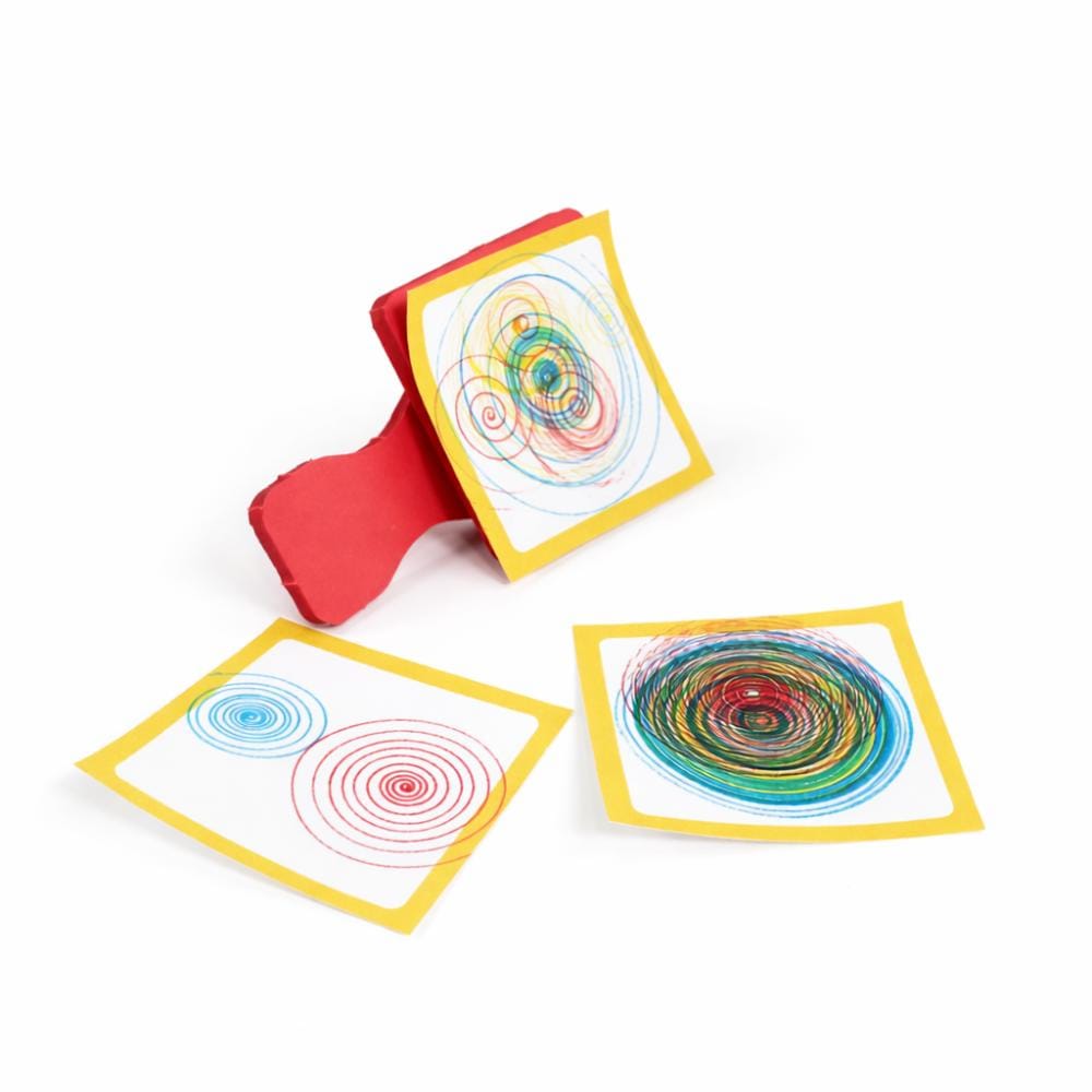 A finished Hypnotizer wind-up drawing machine next to a sticky note covered in a colorful hand-drawn spiral