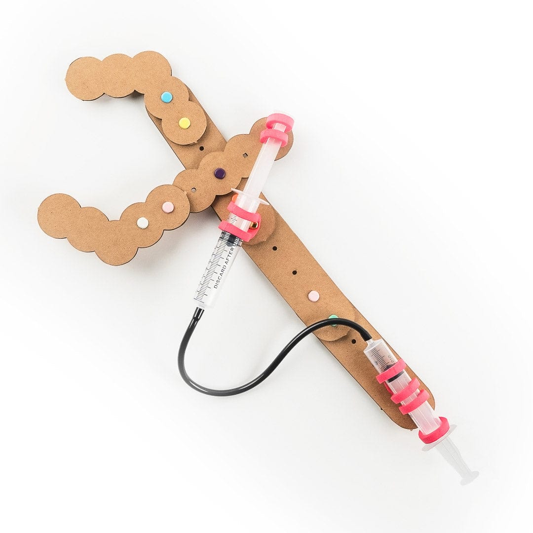 An assembled cardboard Monster Claws pincer decorated with colored dot stickers, connected to two syringe-style pistons by a black connector tube
