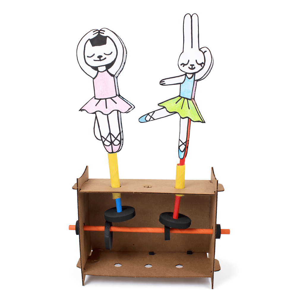 A finished Scene Machines automata: two hand-colored paper figures on straw axles turn above black foam cams, driven by a crank axle running through a cardboard box frame.