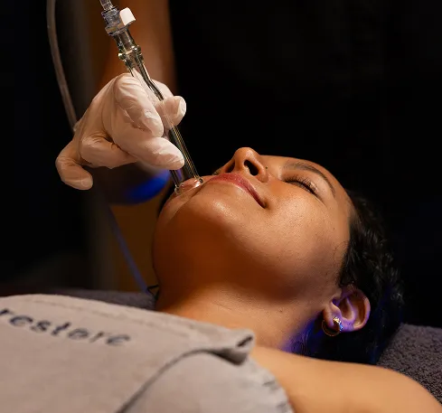 A woman in a Restore towel receives a Hydrafacial