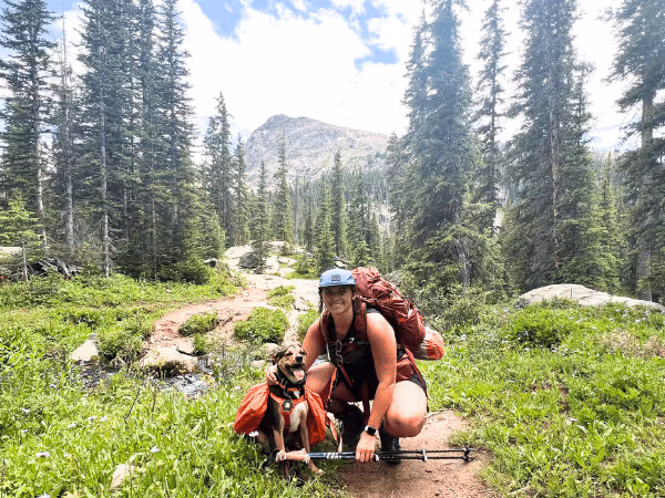 A photo of a pet parent hiking with a dog, complete with all the needed hiking essentials