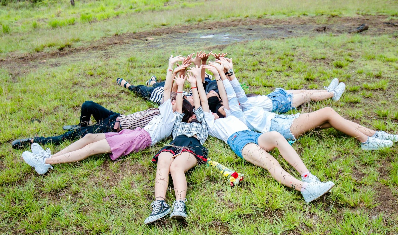 A group of teens lies together in a circle on the grass.