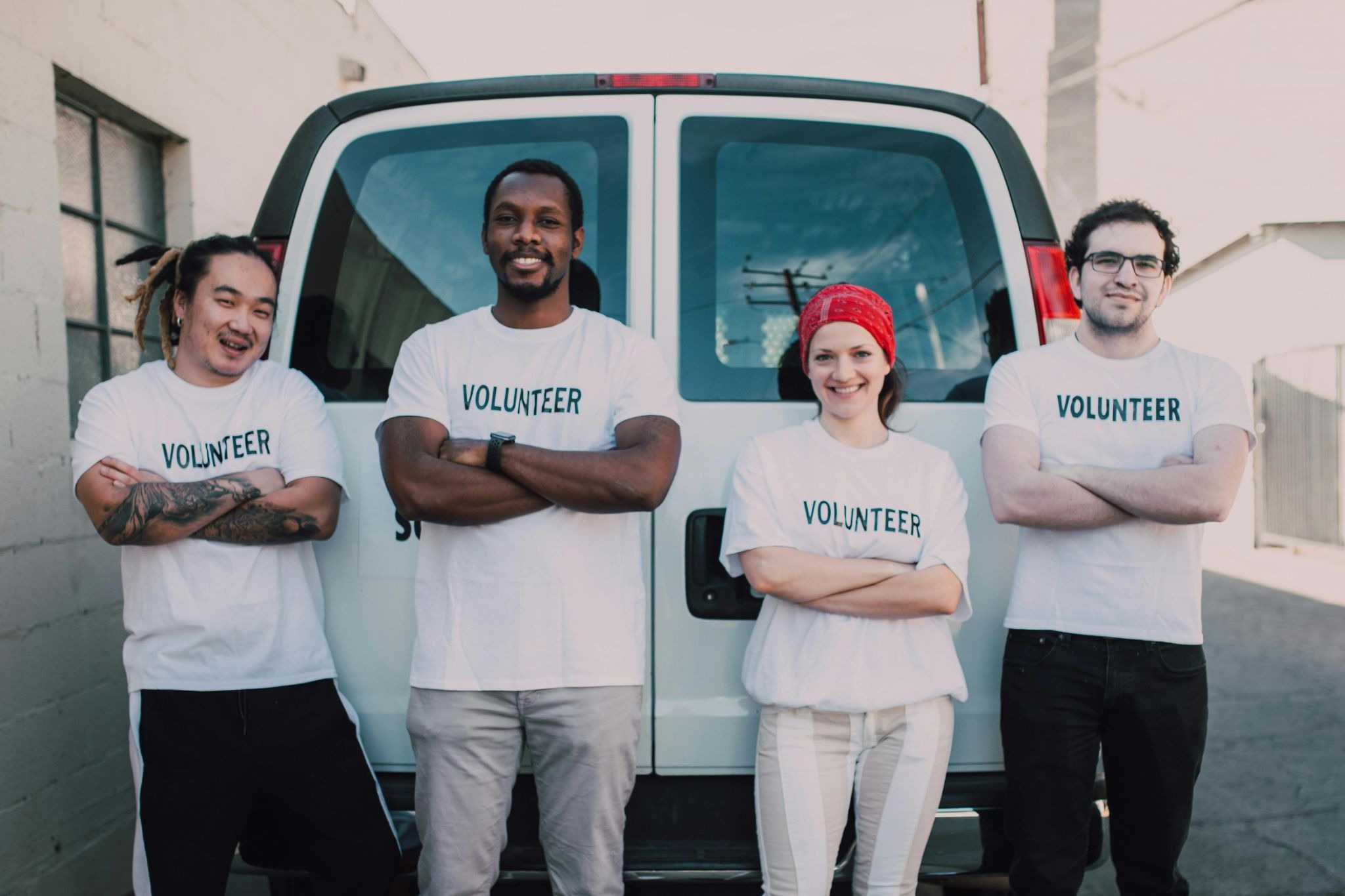 A diverse group of four volunteers smiling in front of a van.