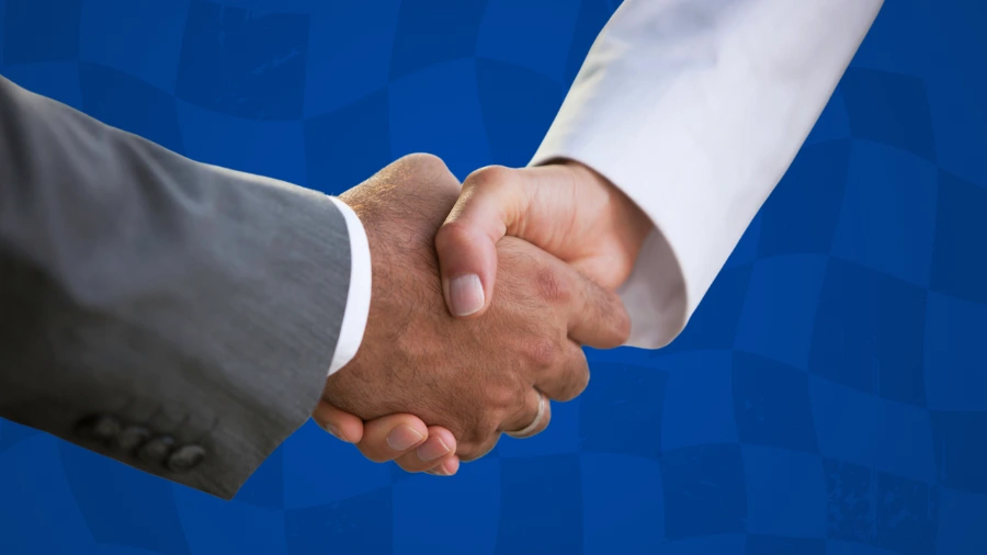 Two people shaking hands, one wearing a gray suit and the other in a white shirt, with a blue checkered background.