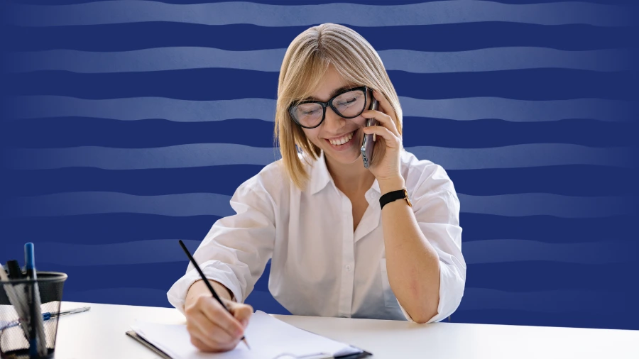 Smiling woman on a phone call taking notes, representing a successful client discovery call.
