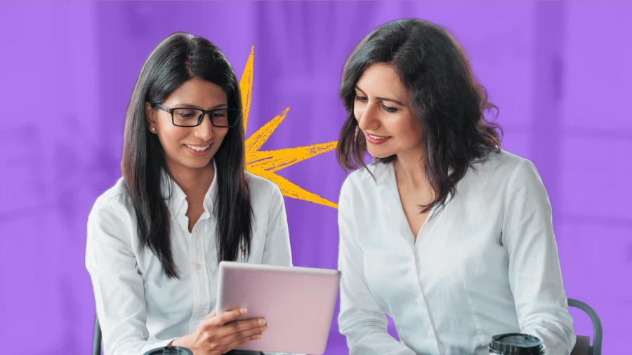 Two women in white shirts smiling while looking at a tablet together, symbolizing teamwork and business growth.