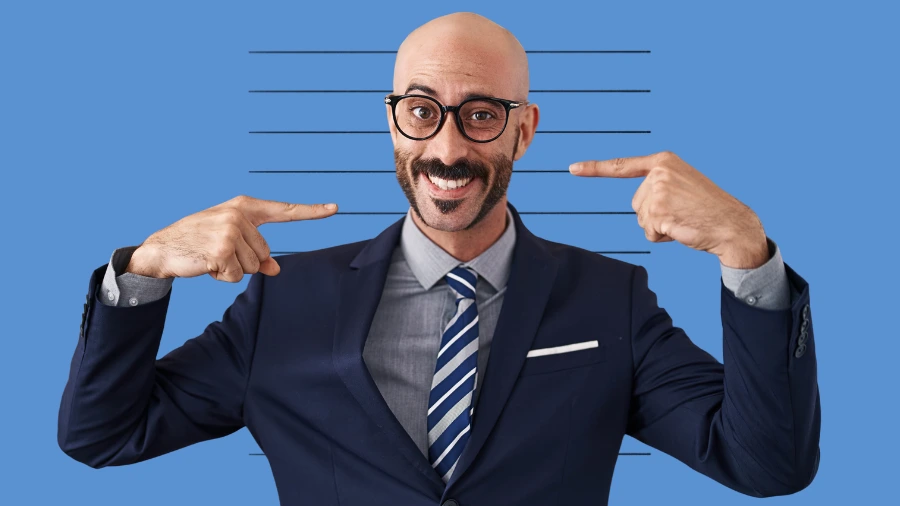 Bald man in business suit pointing at himself with both hands against a blue background with horizontal lines