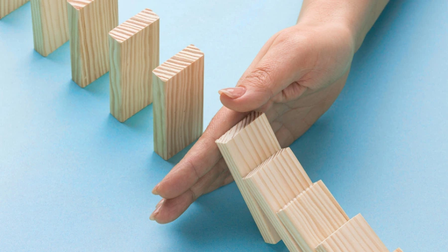 Hand stopping falling wooden blocks, symbolizing preventing business failure and recognizing when a business model needs to change