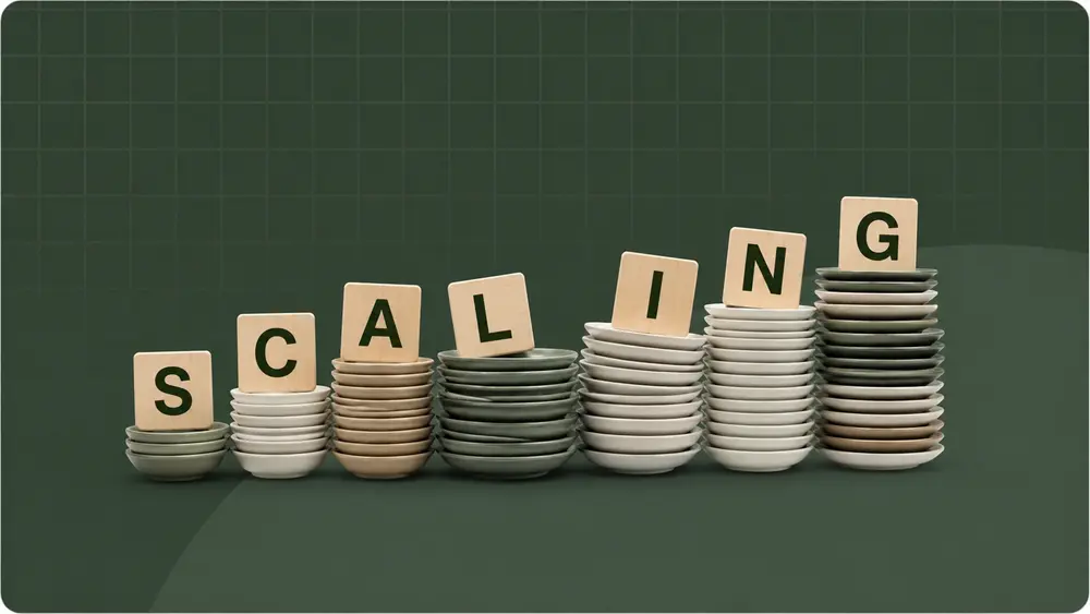 Minimal photography-style thumbnail showing stacked ceramic plates arranged in ascending order with wooden letter blocks spelling ‘SCALING’ on a dark green grid background.