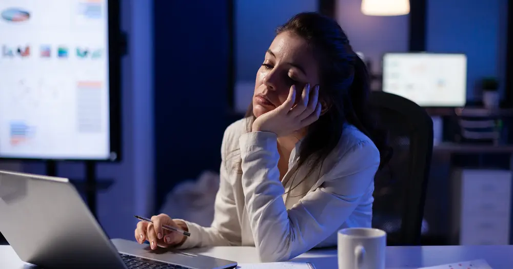 Professional woman looking frustrated while reviewing data on a laptop in a dimly lit office, symbolizing burnout, low performance, or business challenges.