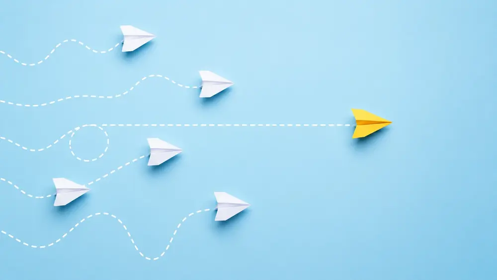 Minimalist illustration of several paper airplanes following different flight paths while one yellow airplane moves directly forward, symbolizing varying levels of buyer readiness and decision-making confidence.