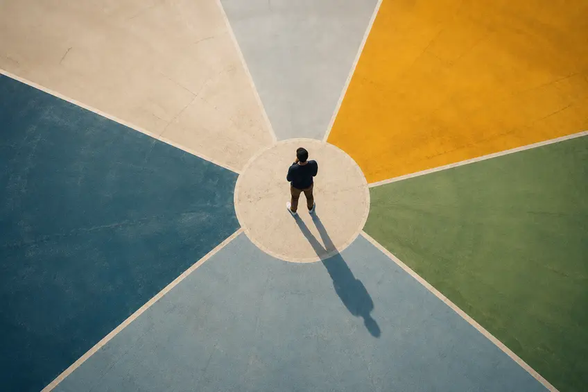 Overhead view of a person standing at the center of colorful geometric paths, symbolizing clarity, strategic direction, and making focused business decisions as a company grows.