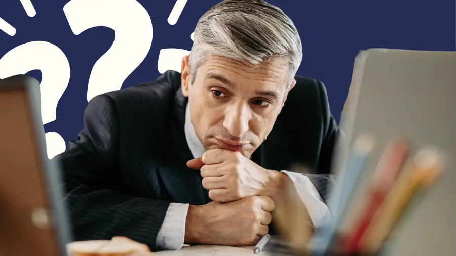 Business professional looking thoughtfully at a computer screen with large question marks in the background, symbolizing uncertainty, decision-making, and business challenges.