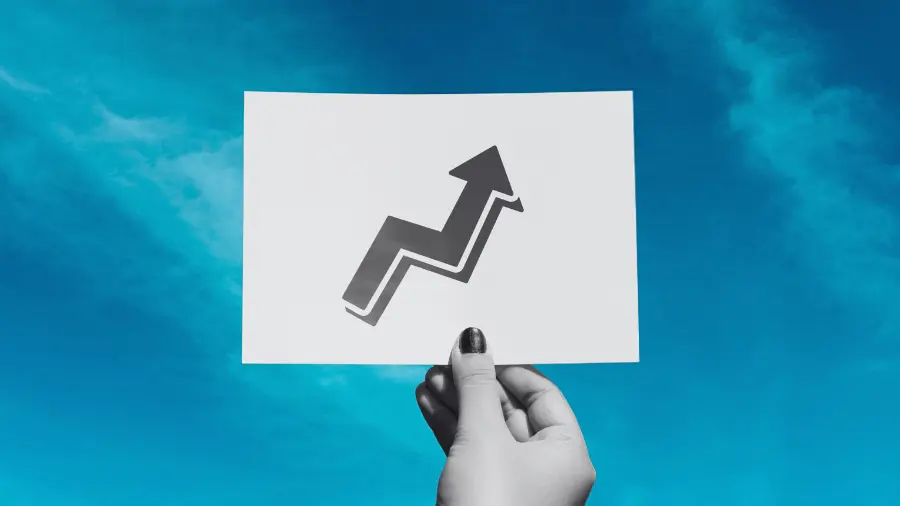 “Hand holding a card with an upward arrow against a blue background, symbolizing business growth.