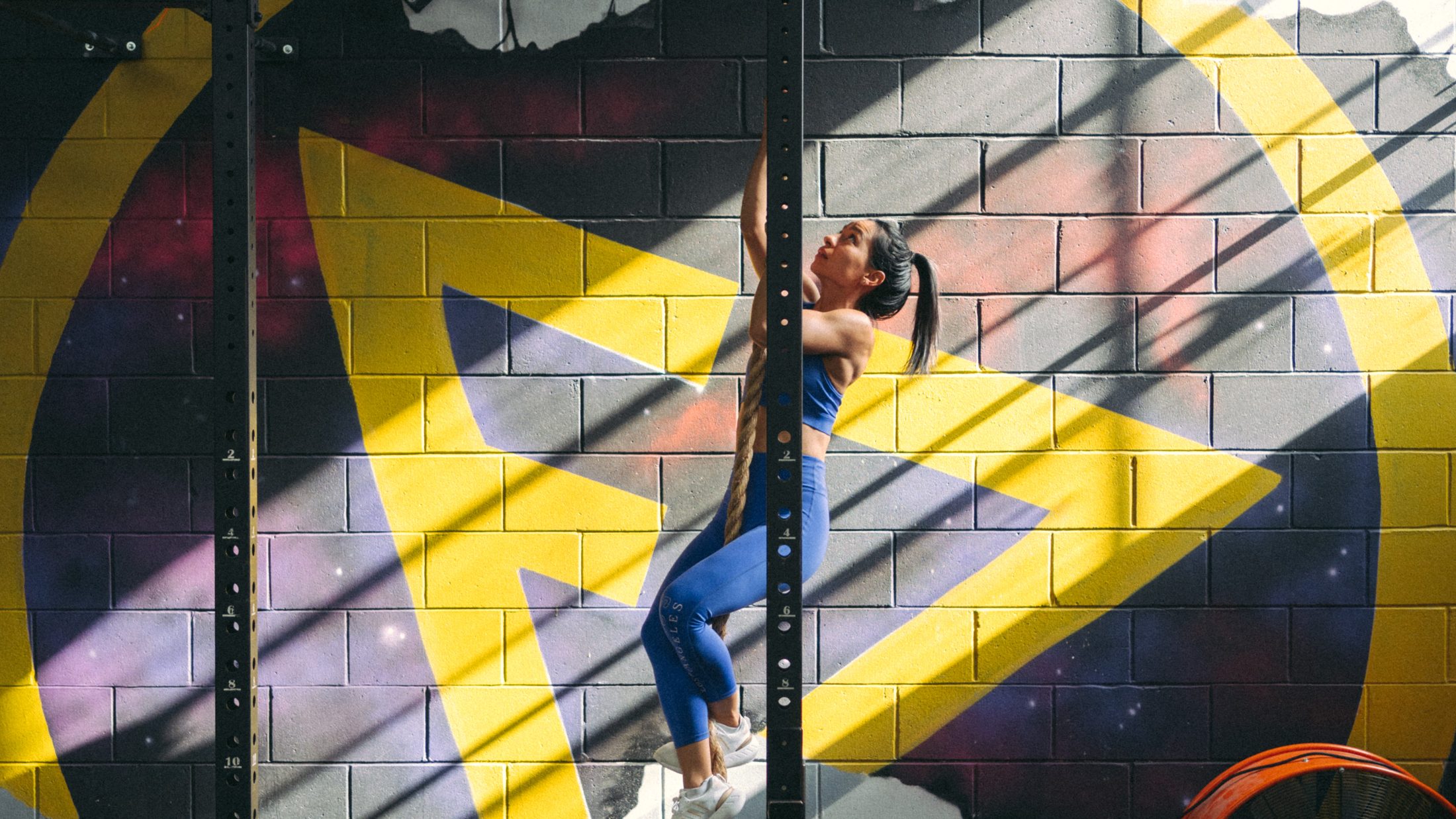 Member climbing the rope in front of the Facet Seven mural