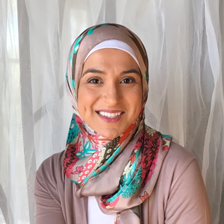 Photo of Marwa Abdalla smiling, White fabric background, Marwa Abdalla is wearing a pink cardigan and pink and teal and  hot pink hijab