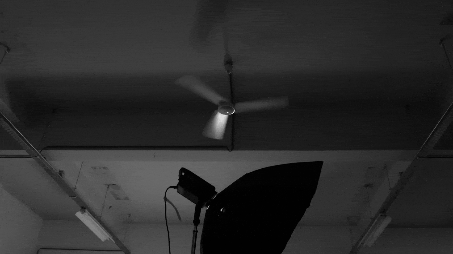 Black and white gif of a ceiling fan spinning with a studio light and diffuser in foreground.