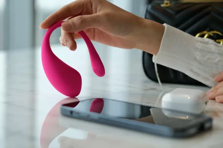 A pink vibrator being held next to a phone indicating it can be controlled by an app