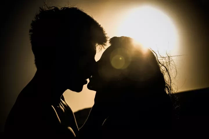 Silhouette of a couple kissing against a bright sunset