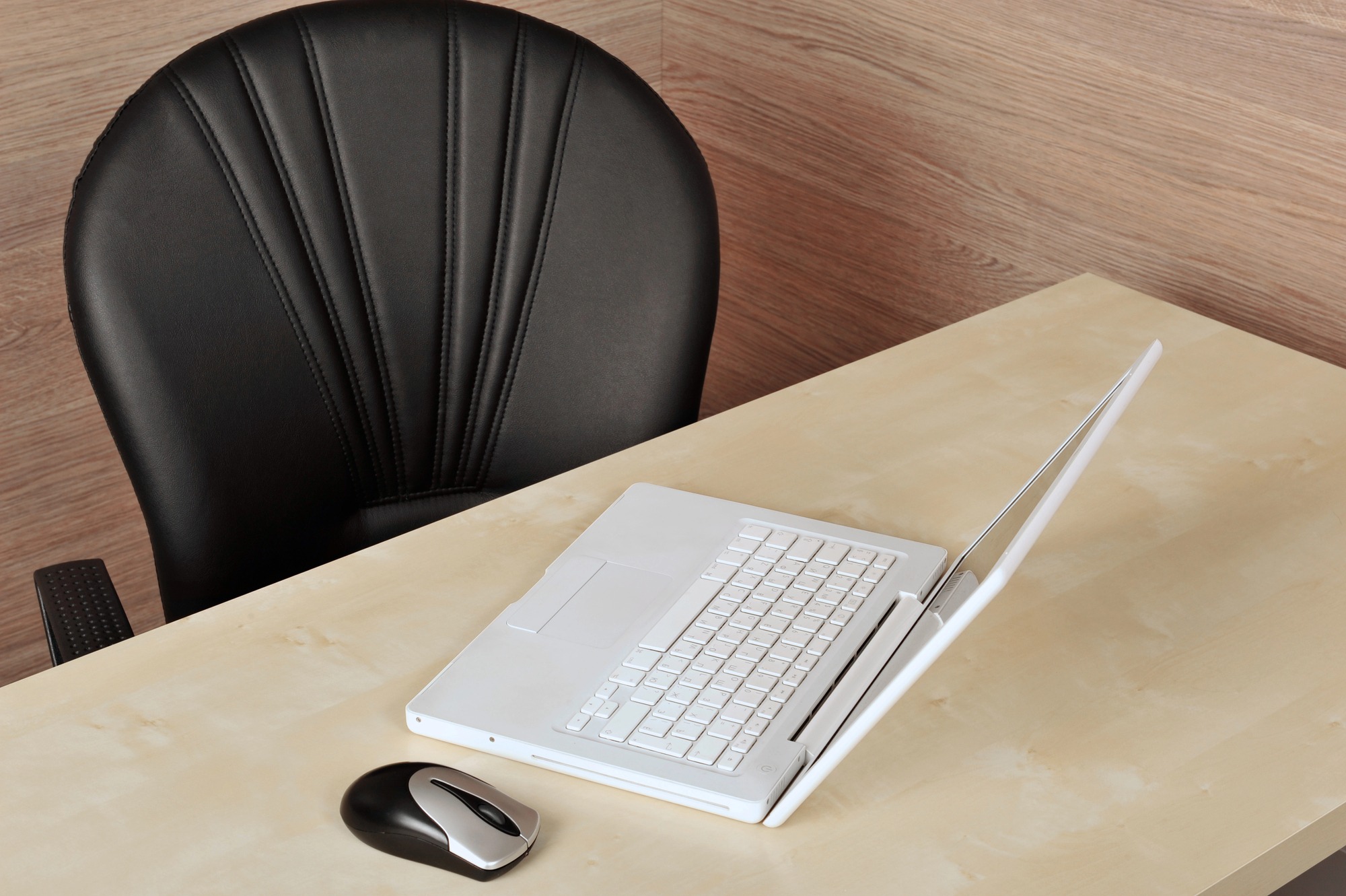 An empty office chair next to an abandoned white laptop.