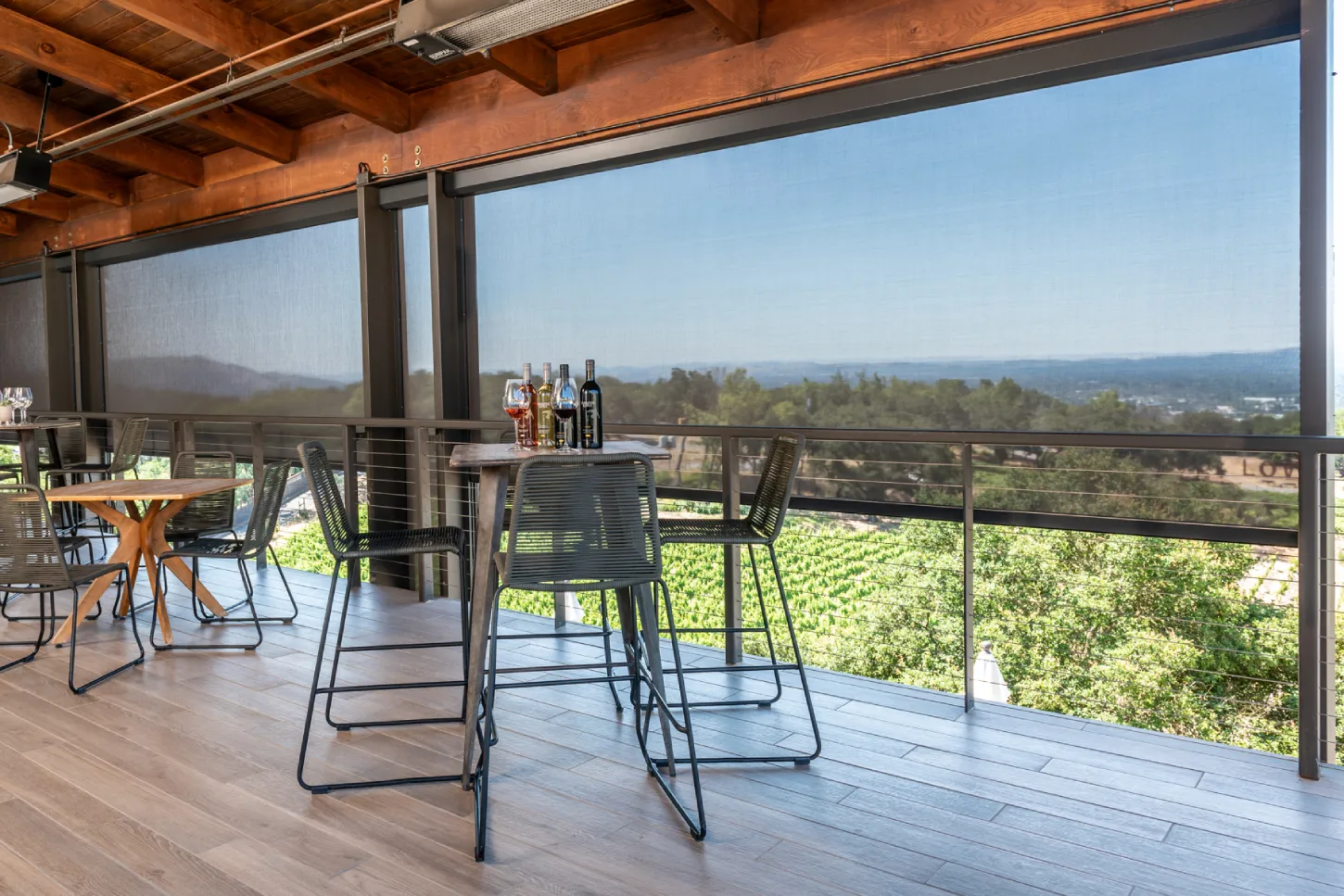Rooftop patio with bar stools and tables, overlooking a scenic view with trees and a distant coastline.