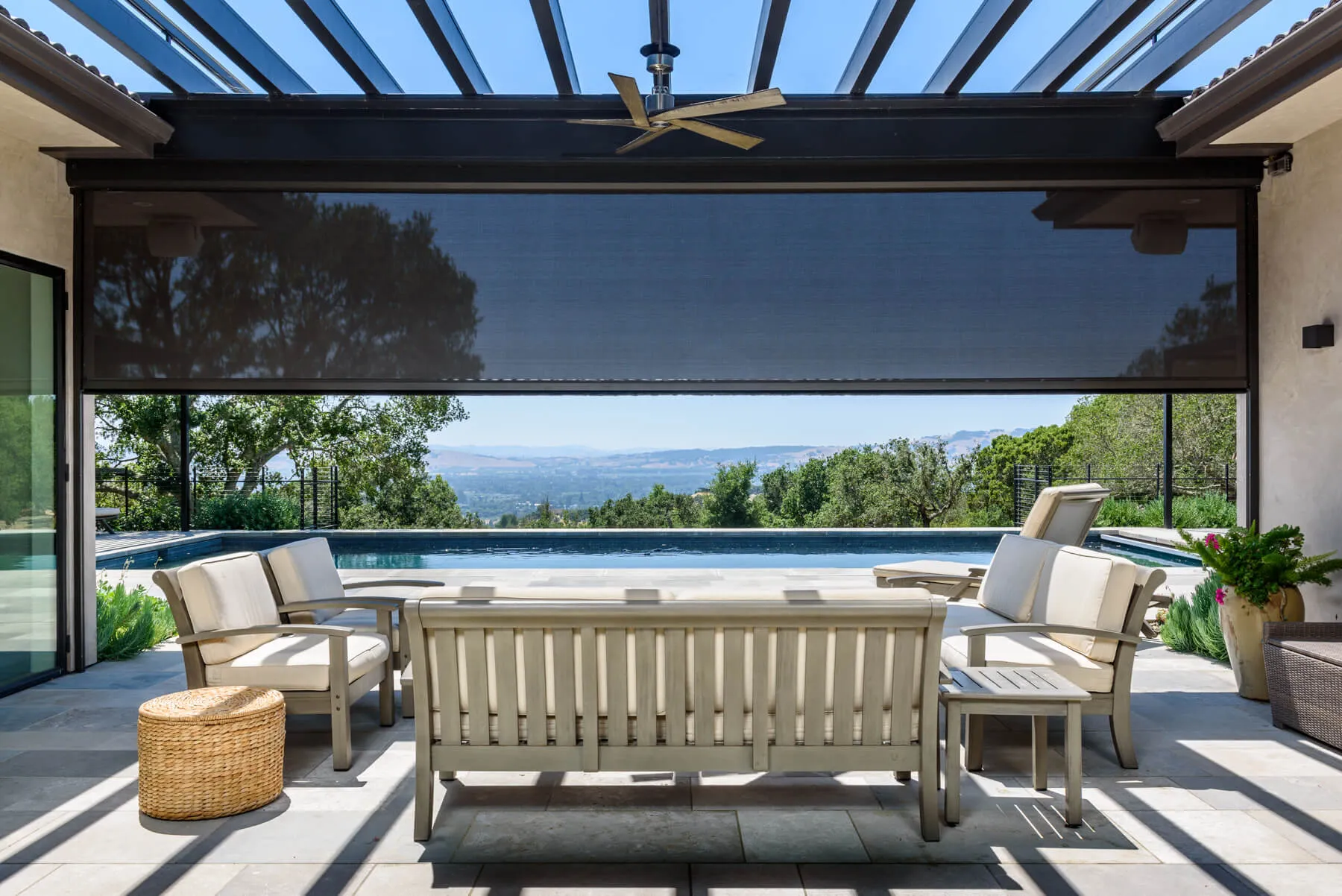 Outdoor patio with seating area, pergola, and view of a pool and landscape in the background.