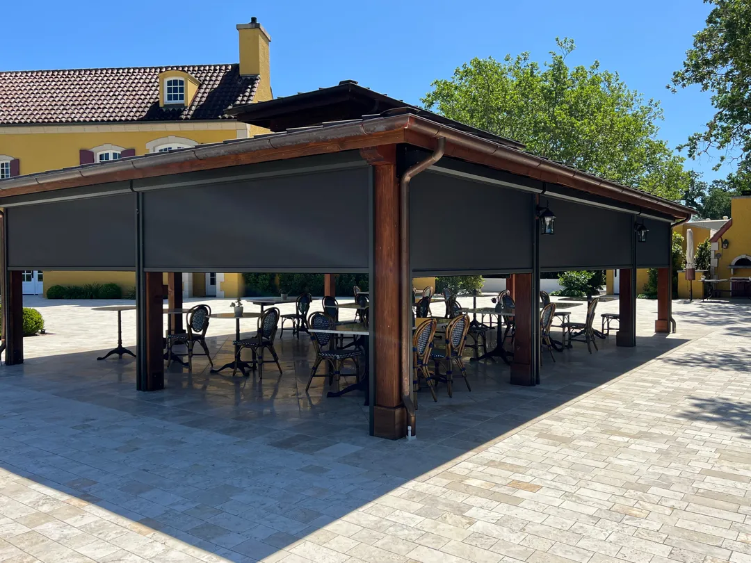 Outdoor patio with retractable awning and tables, surrounded by a yellow building and greenery.