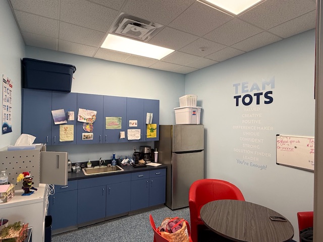 Breakroom at Aqua-Tots Amherst before repainting, showing blue cabinetry and motivational wall graphics.