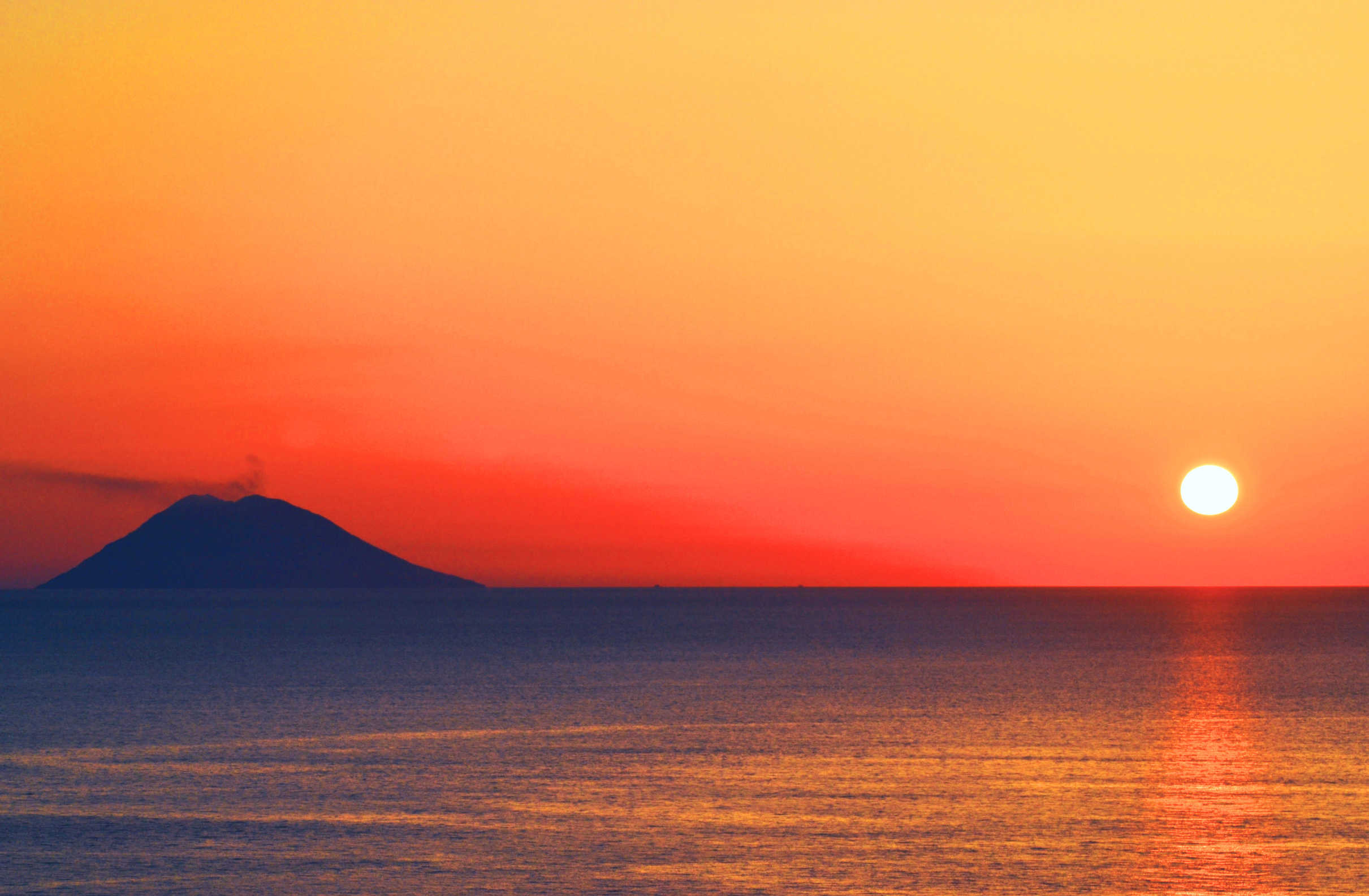 Sun setting over mountain and ocean