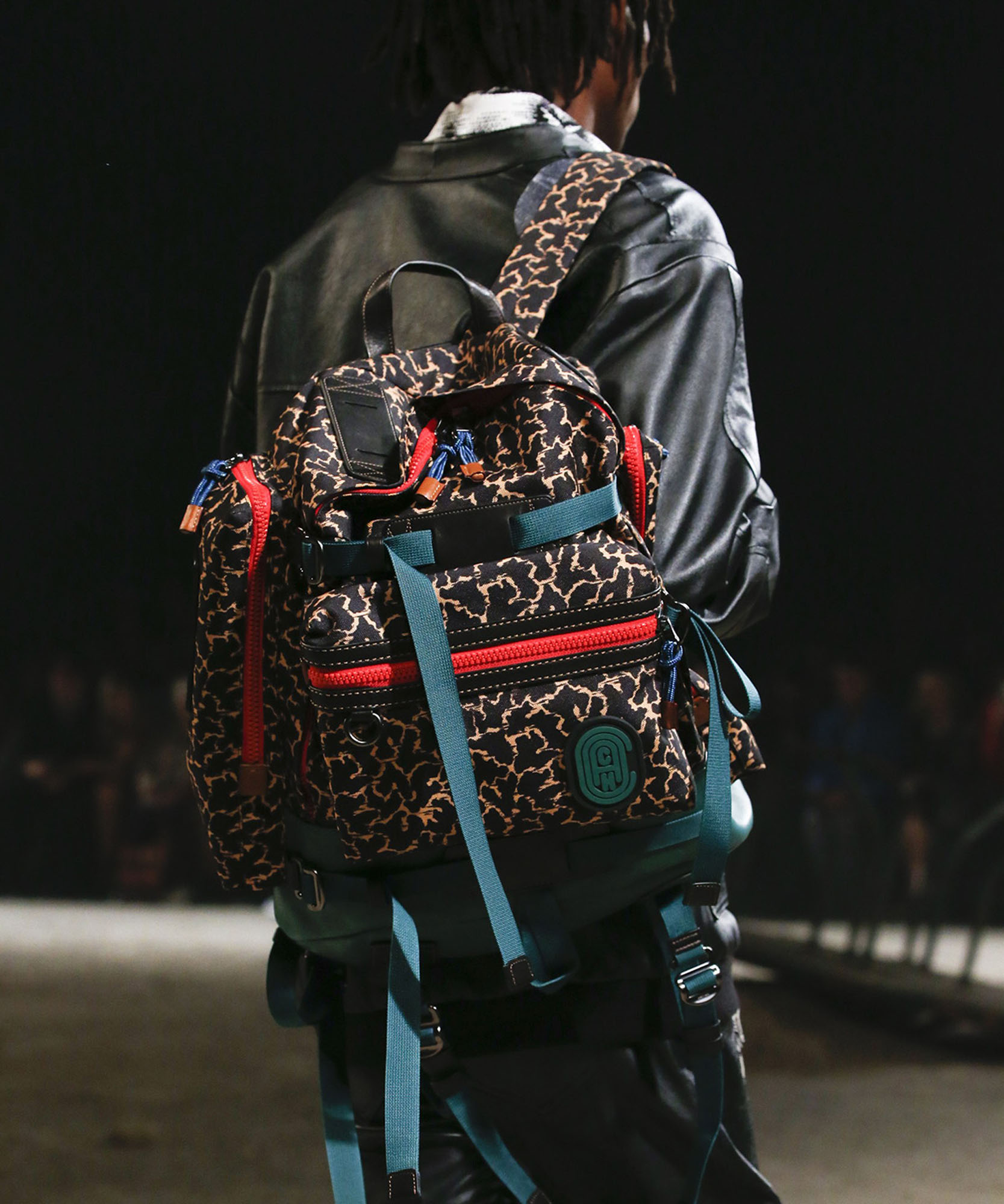 photo of male models backpack wearing a black leather jacket walking down runway