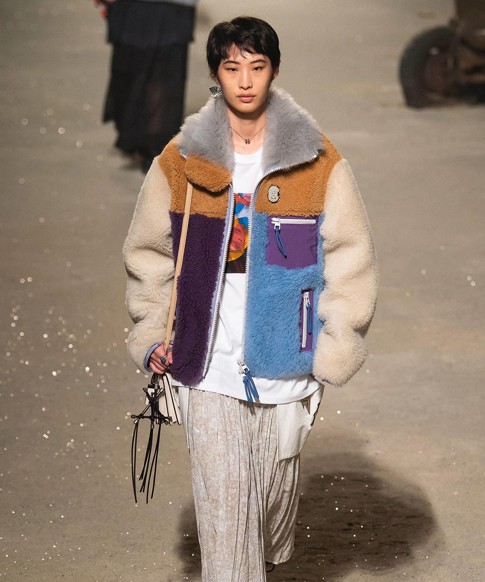 photo of model wearing colorful jacket walking down runway