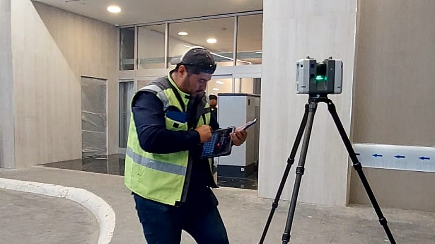 Técnico de Juárez Thompson 3D con una tableta junto a un escáner láser Leica RTC360 sobre trípode, frente al acceso interior de una plaza comercial