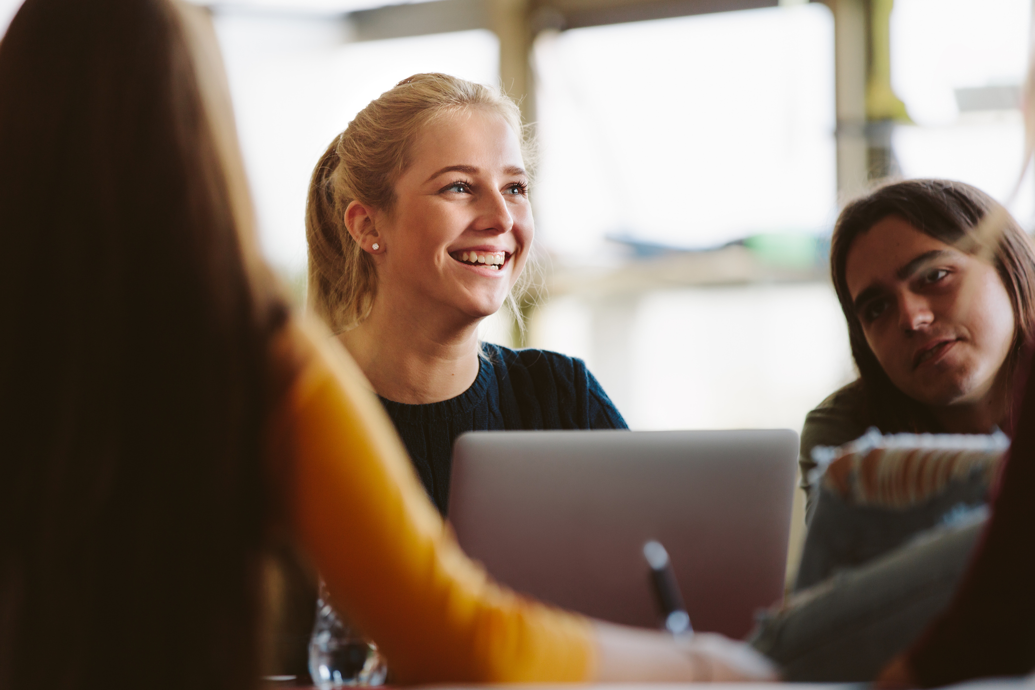 3 female students around a table with computers, including a blonde haired girl in the middle, who is smiling