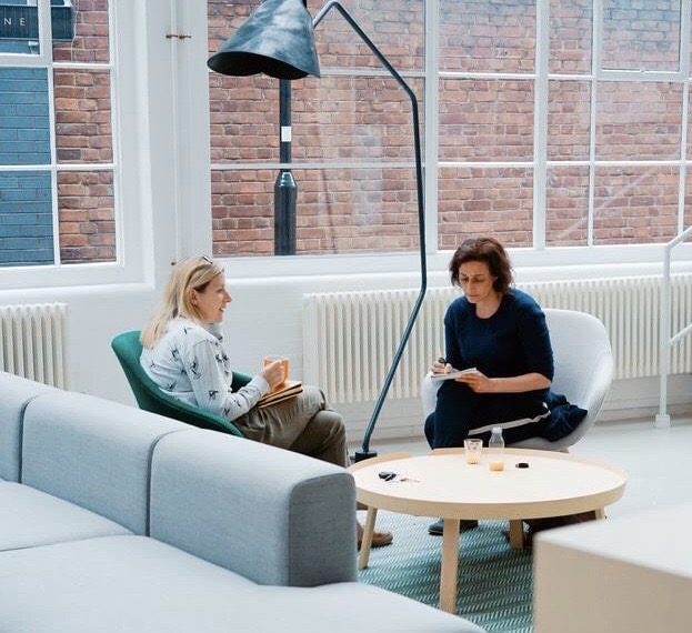 Two middle-aged women including a lecturer discussing an education program in a blue and white room over coffee