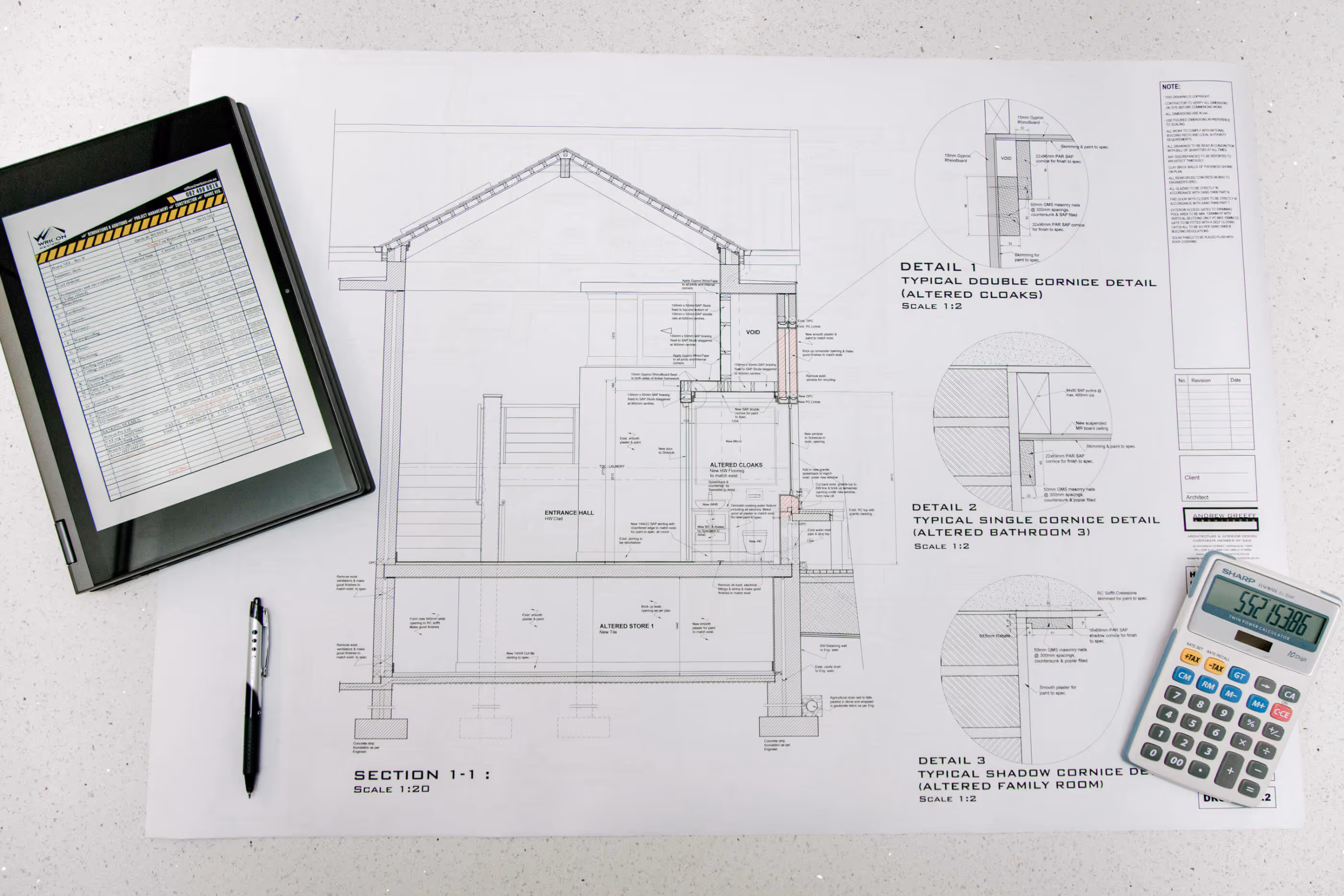 Architectural blueprint drawing on white table with a pen, a tablet displaying a document, and a calculator.