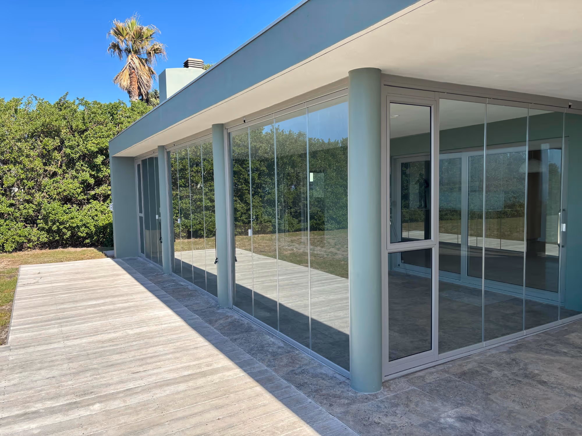 Modern house exterior with large glass sliding doors and a stone-tiled patio under a clear blue sky. Work by Wricon construction.
