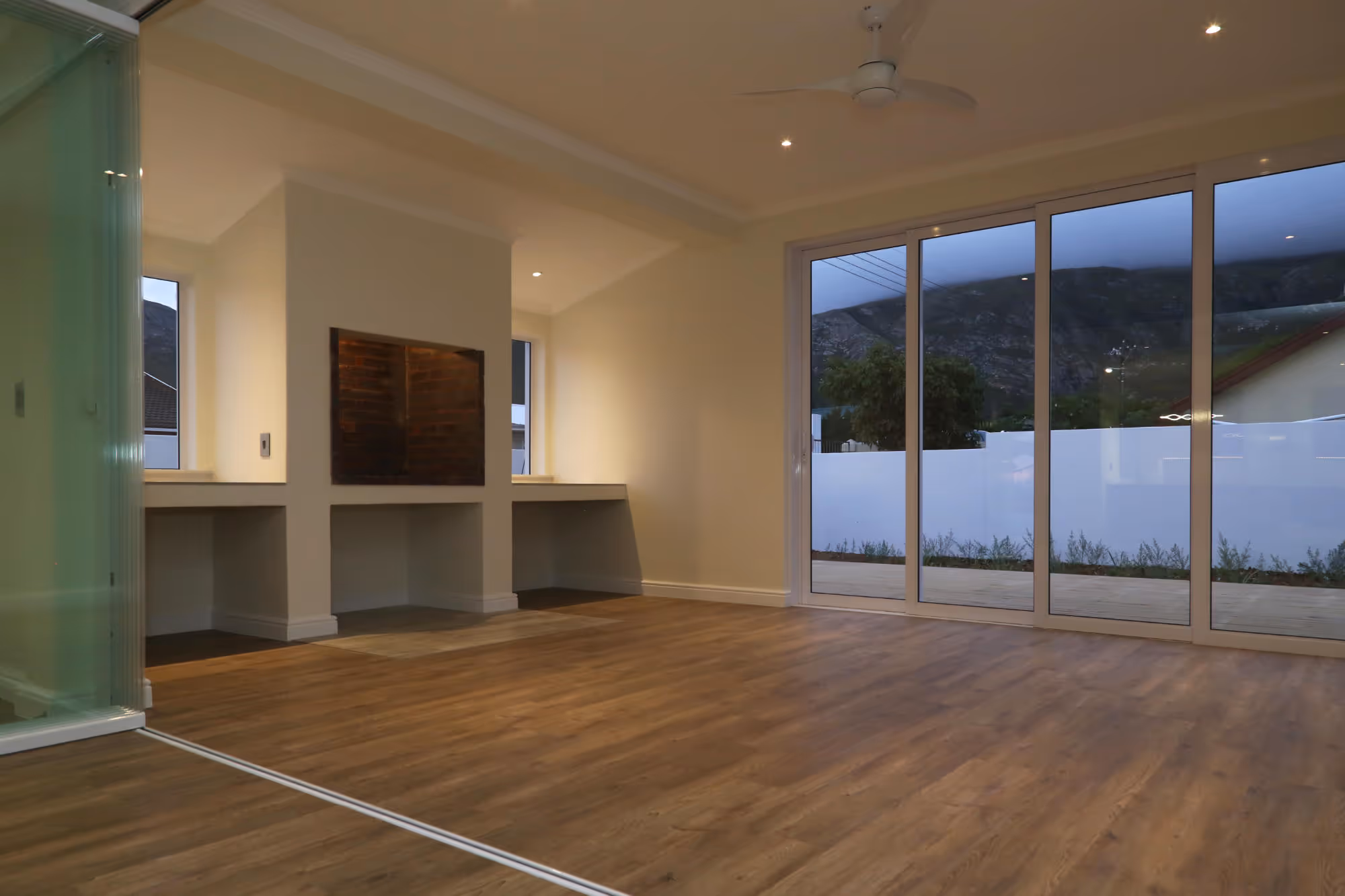 Empty modern living room with wood flooring, built-in fireplace, and large sliding glass doors showing mountain view outside. Work by Wricon construction.