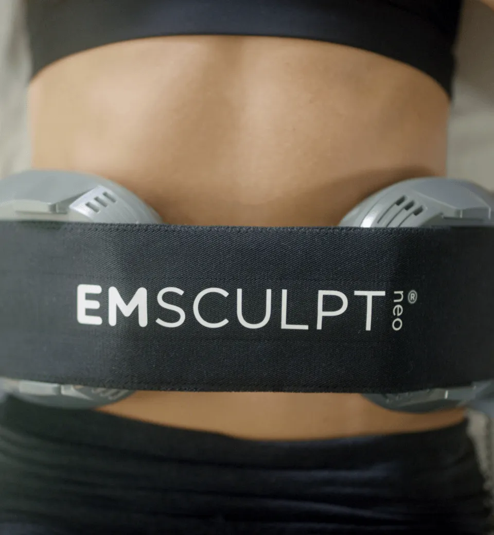 EMSCULPT NEO device strapped to a person's abdomen during a muscle toning and fat reduction procedure.