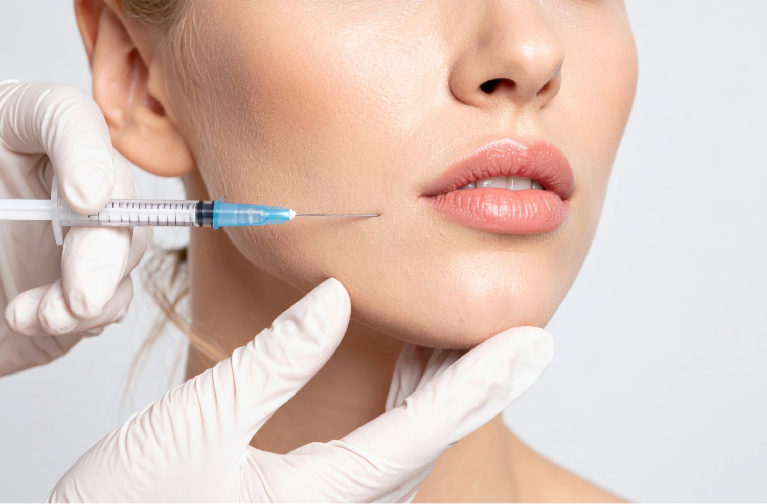 Close-up of a woman's lower face receiving an injection near the cheek from a gloved hand holding a syringe.