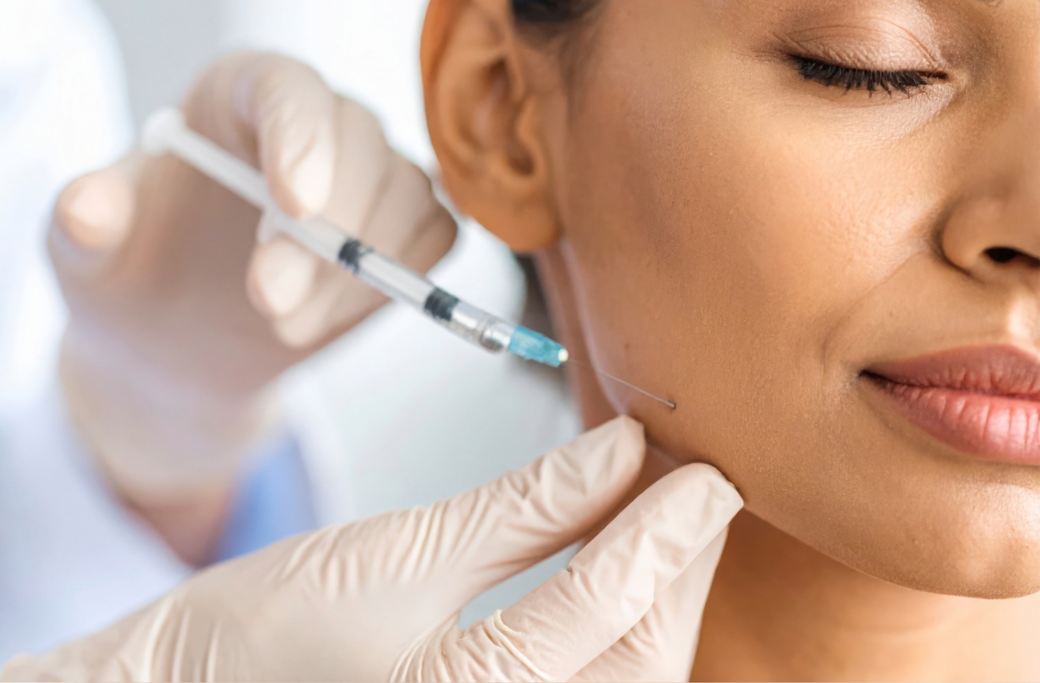 Close-up of a healthcare professional wearing gloves injecting a needle into a woman's cheek near her jawline.