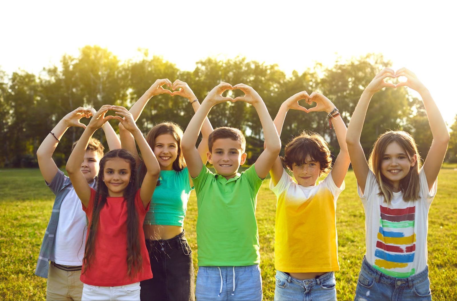 Group of happy children in a park smiling and making heart gestures