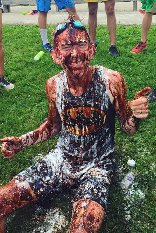 Zach smiling and showing a thumbs up after messy games, totally covered in chocolate syrup.