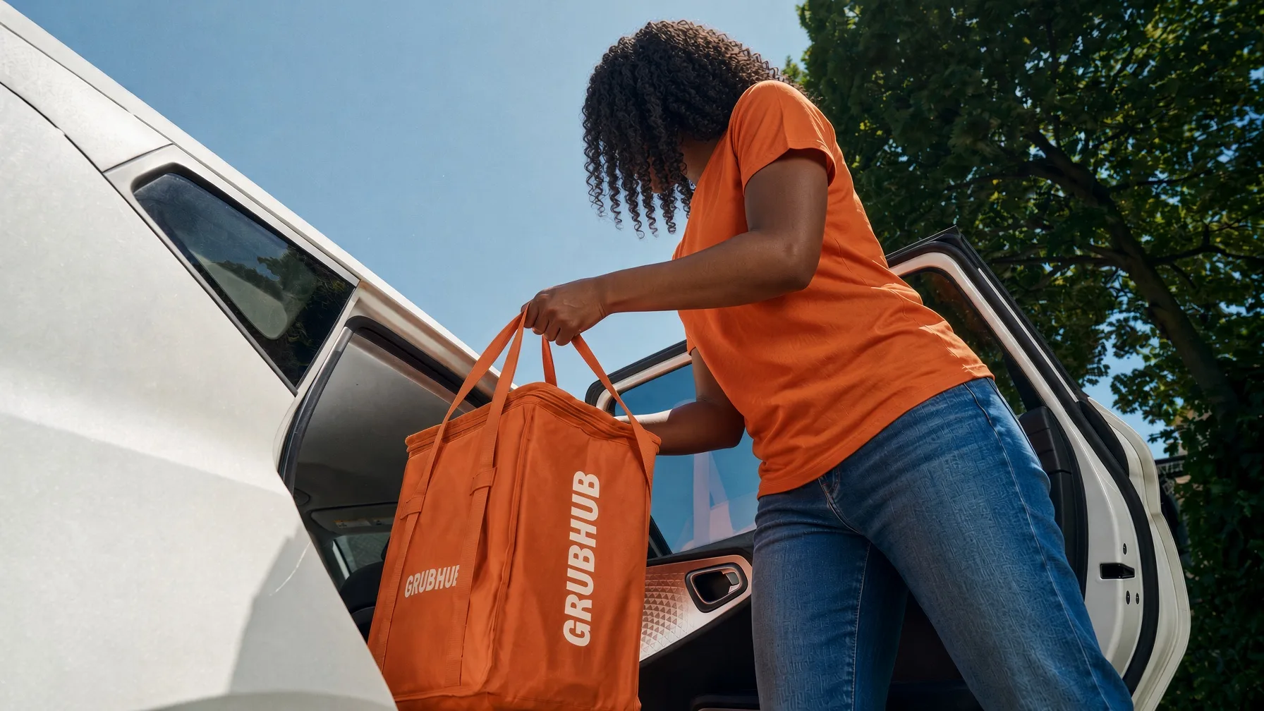 A Grubhub courier lifting an orange insulated Grubhub bag out of a white car
