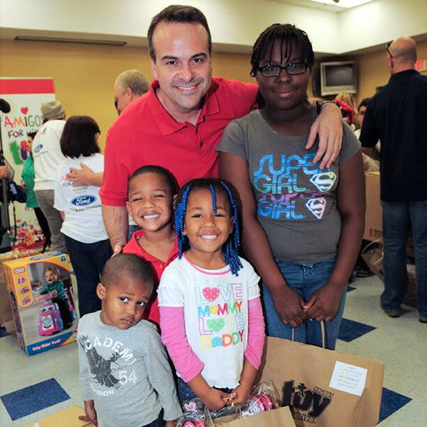 AFK founder, Jorge A. Plasencia, smiling with a mother with their children, holding bags in a community event space.