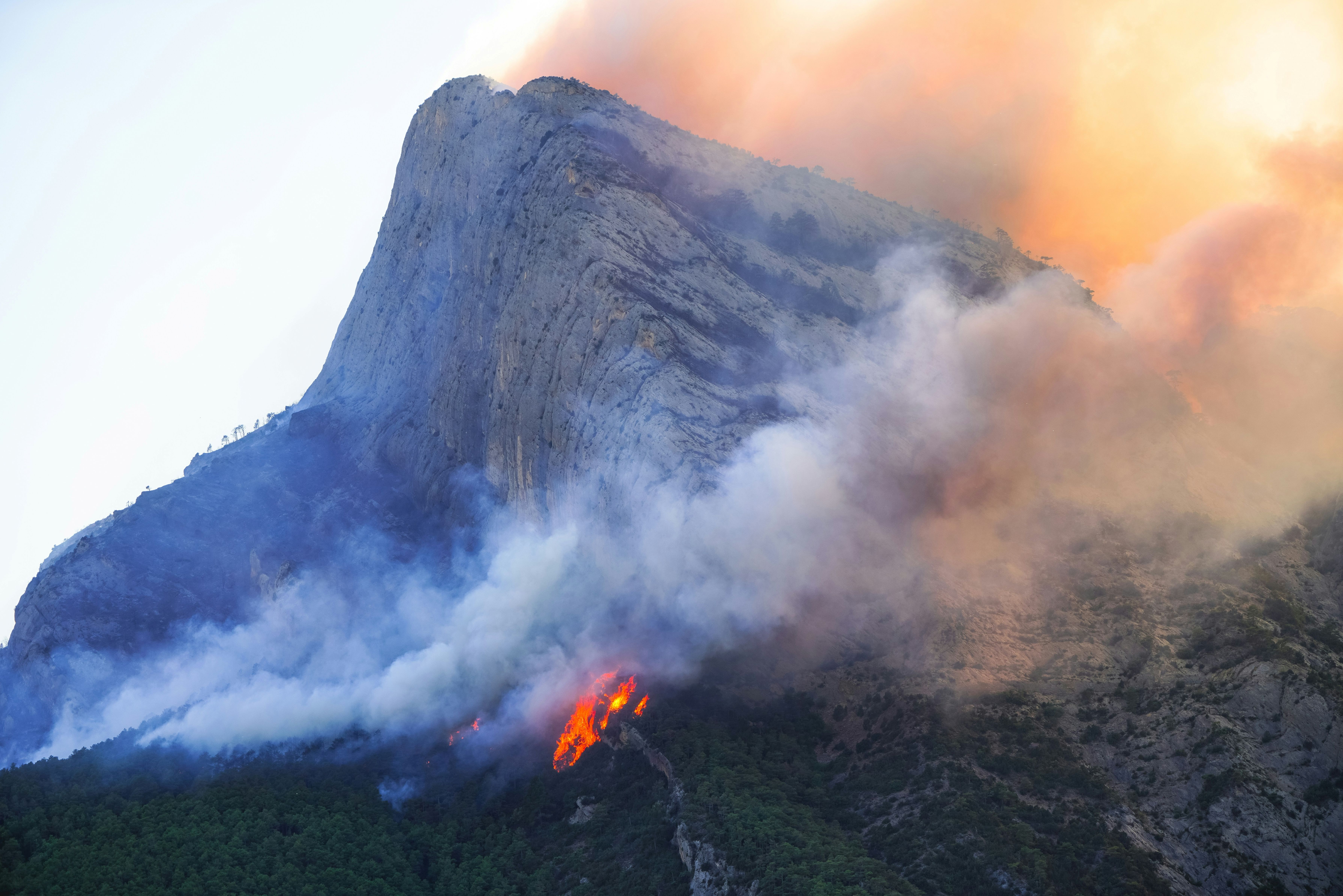 A wildfire on the side of a mountain at dusk.